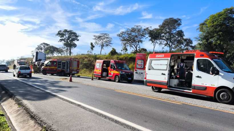 Veículo de emergência e ambulâncias parados em uma rodovia, com árvores ao fundo e céu claro.