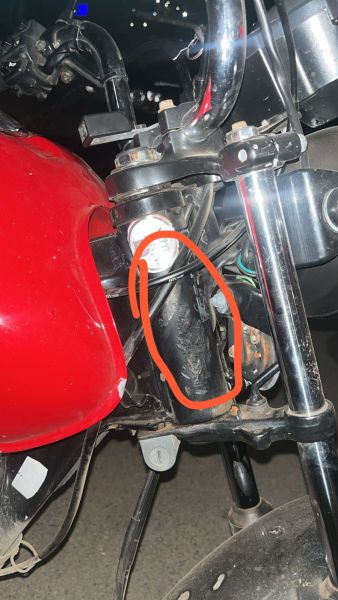 Close-up de um componente mecanico de uma motocicleta, com destaque para um tubo escuro em meio a outras partes metálicas e um tanque vermelho.