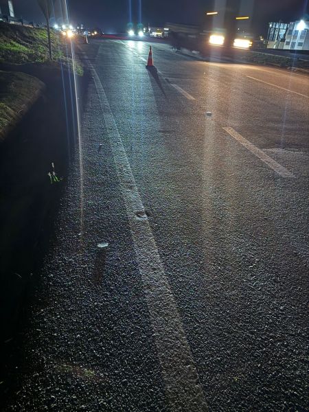 Imagem da estrada à noite, com marcas na pista e um cone laranja no centro.
