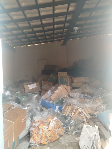 Interior de um depósito bagunçado, com caixas e embalagens espalhadas pelo chão.