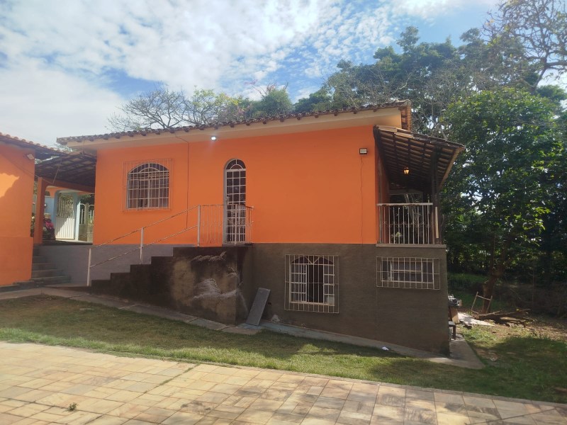 Casa de parede laranja com varanda, jardim e escadas externas em um dia ensolarado.