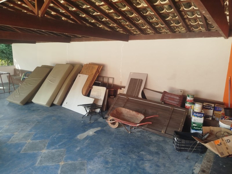 Uma área de armazenamento com colchões, pranchas de madeira, uma carroça e caixas de materiais diversos.