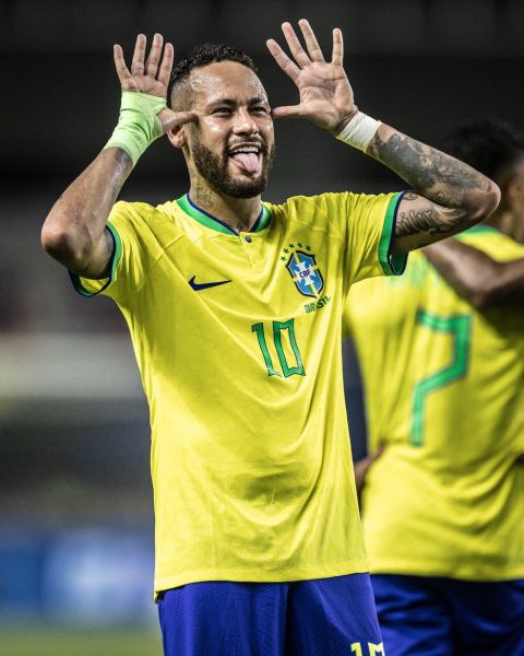 A Brazilian soccer player in a yellow jersey with the number 10 celebrates with a playful expression, sticking out his tongue and making a gesture with his hands.
