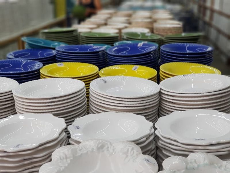 Pilhas de pratos coloridos e brancos empilhados em uma loja, com foco em uma variedade de estilos e tamanhos.