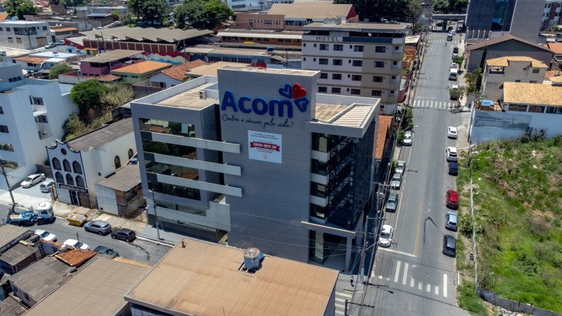 Imagem aérea do prédio da Acom, localizado em uma área urbana, com diversas casas e edifícios ao redor.