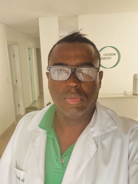 A person wearing glasses and a white lab coat, standing inside a medical facility.