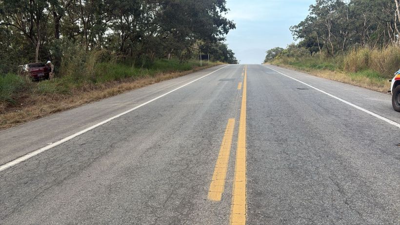 Vista de uma estrada asfaltada com faixa amarela ao centro, ladeada por vegetação ao lado.