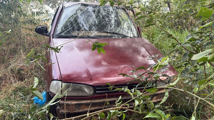 Carro vermelho abandonado coberto por folhas e vegetação.