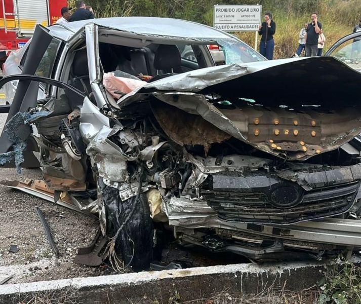 Carro gravemente danificado após um acidente, com a estrutura frontal comprometida e materiais expostos.