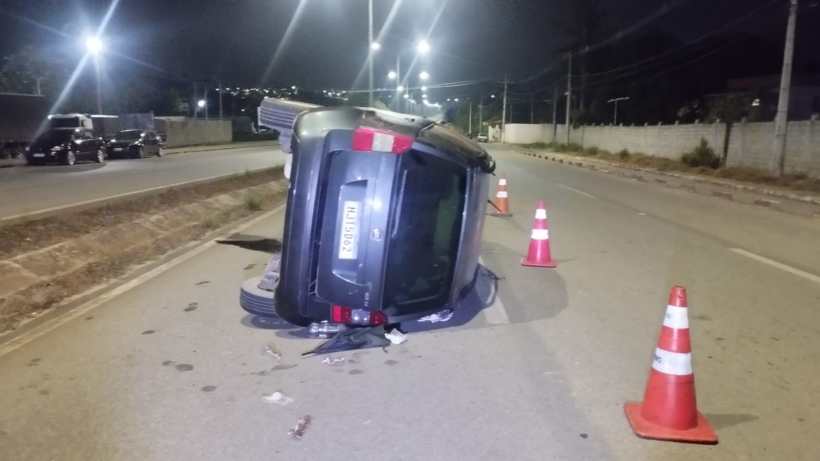 Veículo capotado na estrada à noite, com cones de sinalização ao redor.