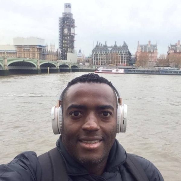 A man wearing headphones takes a selfie in front of the Thames River, with Big Ben partially covered in scaffolding and the Houses of Parliament in the background.