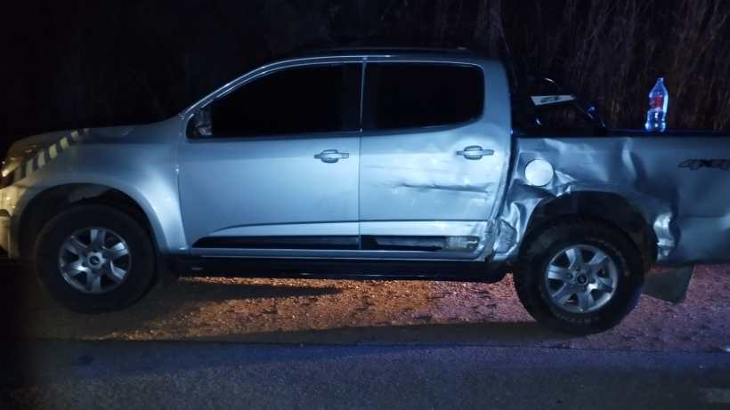 Um veículo pick-up prata estacionado à noite, apresentando danos significativos na lateral traseira direita.
