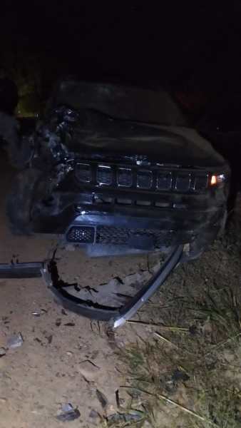 Veículo preto com a frente danificada em estrada de terra durante a noite.