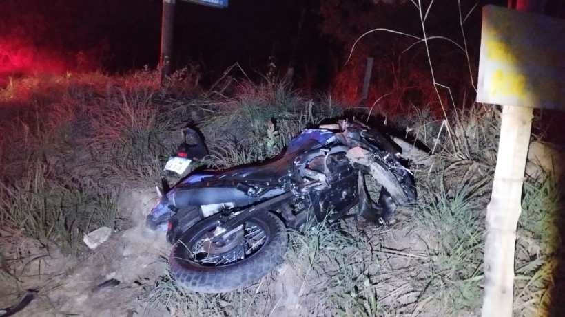 Uma motocicleta caída em um terreno com grama, à noite, com sinais de danos visíveis.