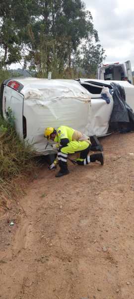 Um veículo capotado em uma estrada, com um socorrista agachado ao lado, avaliando a situação.