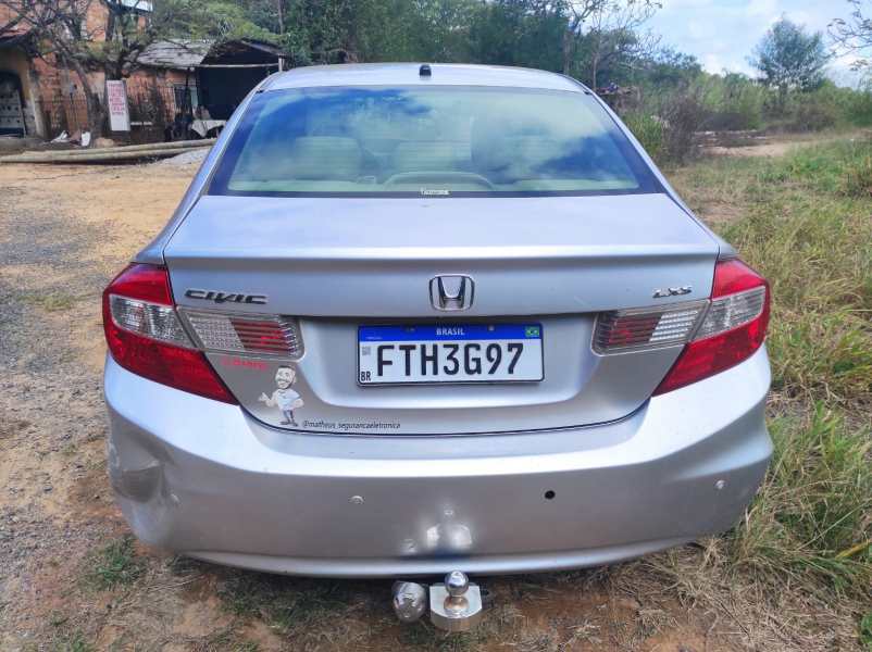 Parte traseira de um carro Honda Civic prata estacionado em um ambiente aberto, com um gramado e algumas árvores ao fundo.