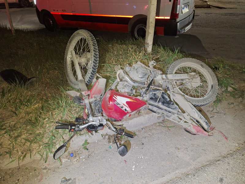 Uma motocicleta caída sobre o gramado, com um pneu para cima e visivelmente danificada.
