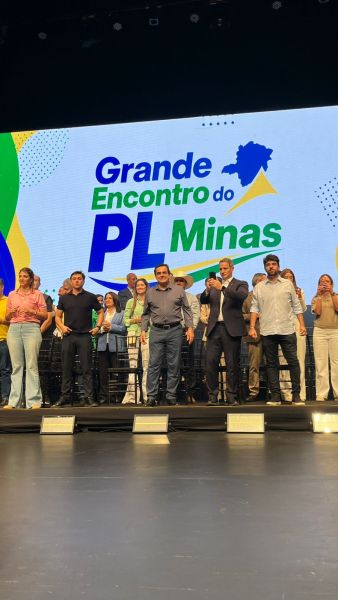 Evento 'Grande Encontro do PL Minas' com grupo de pessoas em um palco, ao fundo uma tela com o nome do evento.
