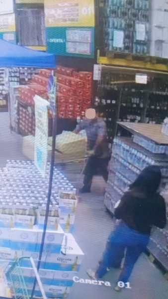 Câmera de segurança de um mercado mostrando duas pessoas: uma empurrando um carrinho e outra em frente a prateleiras de produtos.