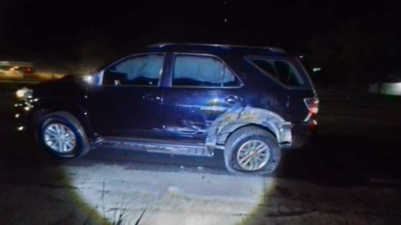 Veículo SUV preto danificado à noite, com marcas visíveis de batida na lateral.