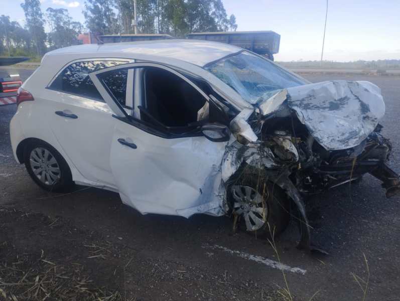 Carro branco danificado em acidente, com o lado frontal amassado e uma porta aberta.