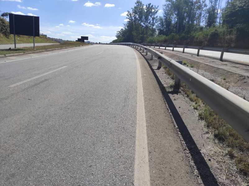 Vista de uma estrada com guard-rail à direita e sinalização em câmbio ao fundo em um dia ensolarado.