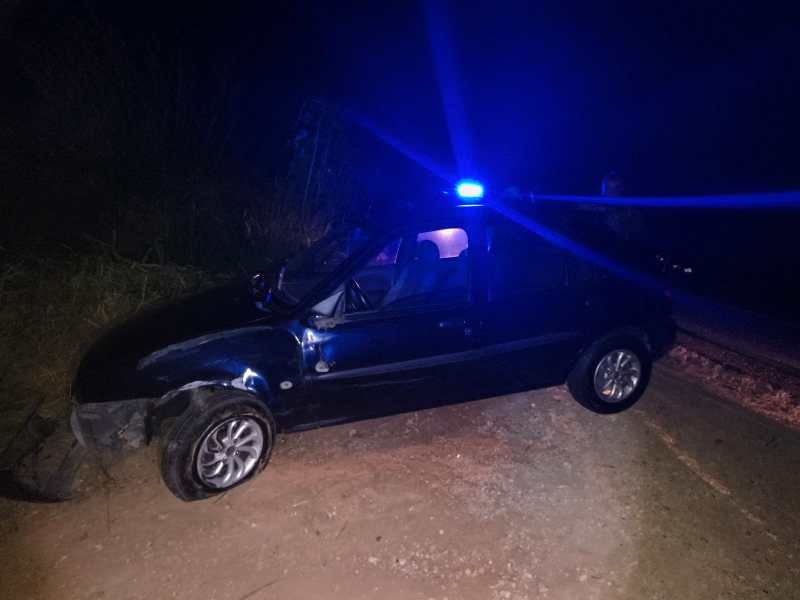 Carro preto envolvido em acidente à noite, com luzes azuis piscando no topo.