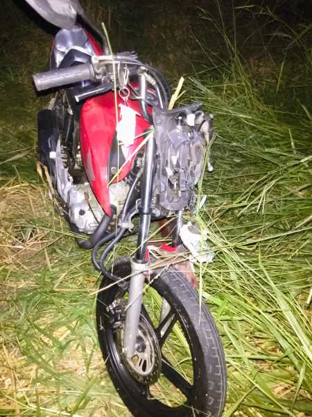 Motocicleta vermelha parcialmente escondida pela grama alta durante a noite.
