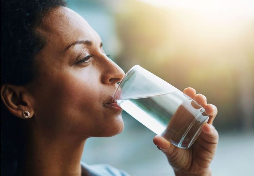Woman drinking a glass of water with a thoughtful expression.