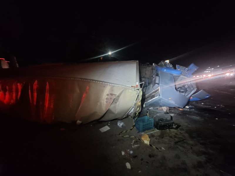 Caminhão acidentado deitado na pista, com visibilidade reduzida devido à noite e iluminação de emergência.