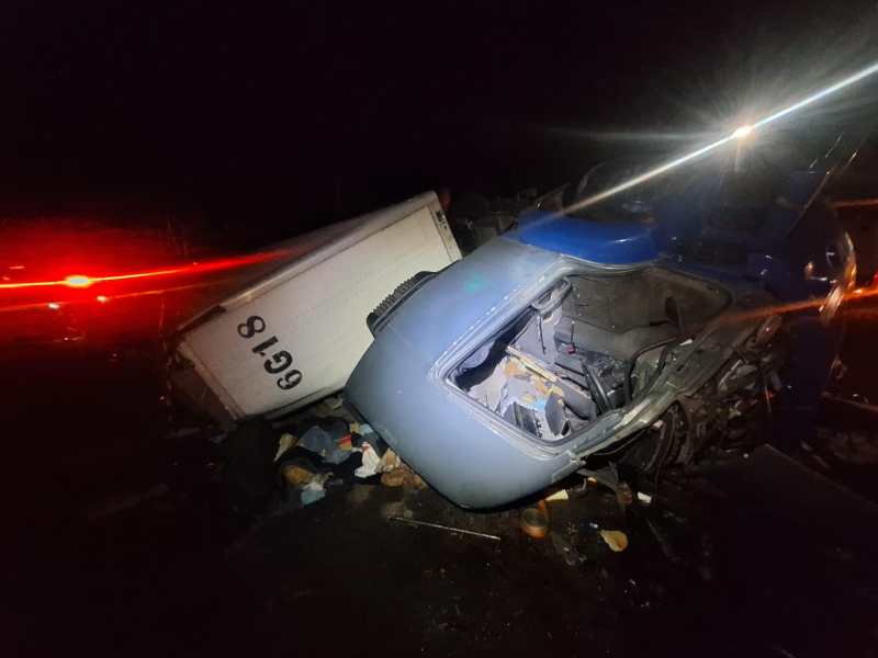 Caminhão envolvido em acidente, tombado ao lado da estrada à noite, com destroços e objetos espalhados ao redor.