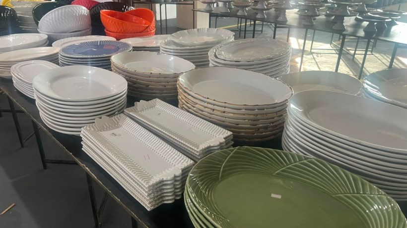 An array of various plates and platters stacked on tables, including white, green, and colorful dishware, arranged in an organized manner.