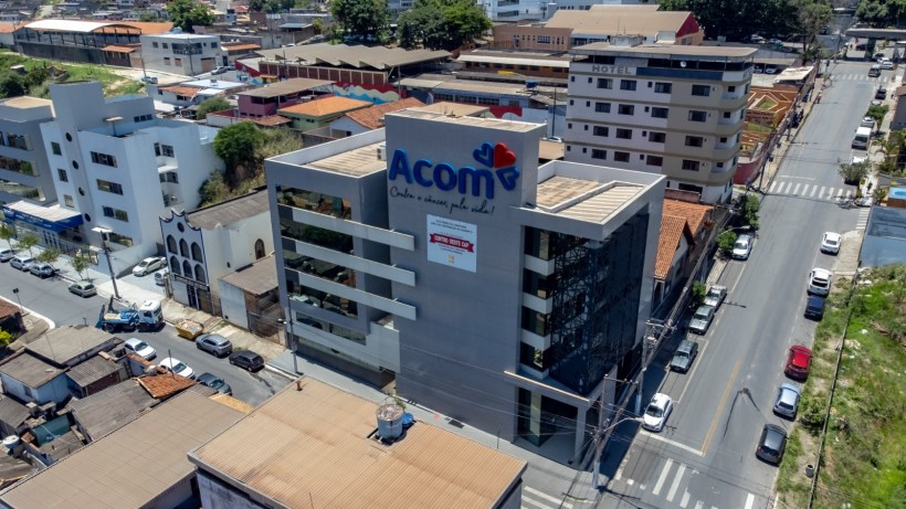 Aerial view of a multi-story building with the sign 'Acom' prominently displayed, surrounded by various smaller structures and vehicles on the street.