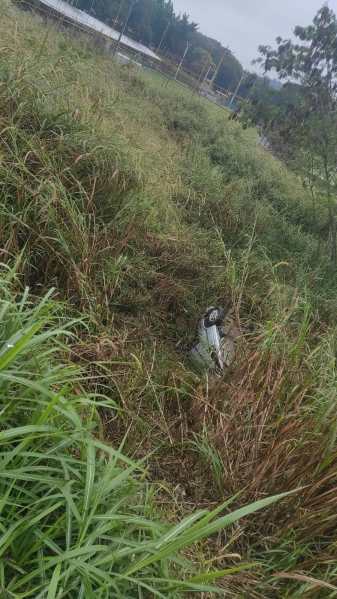 Um carro parcialmente coberto por grama alta em uma área descampada.