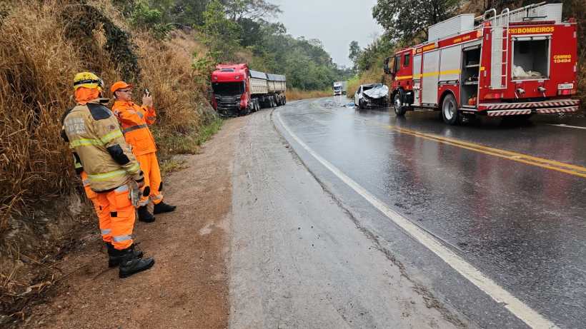 Caminhoneiros e bombeiros em ação em um acidente na estrada, com veículos danificados e chuva.
