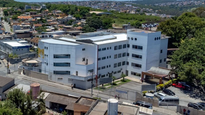 Vista aérea de um edifício branco em uma área urbana, cercado por casas e árvores.