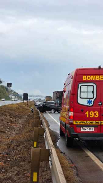 Um veículo acidentado ao lado da rodovia, com uma viatura dos bombeiros estacionada próxima.