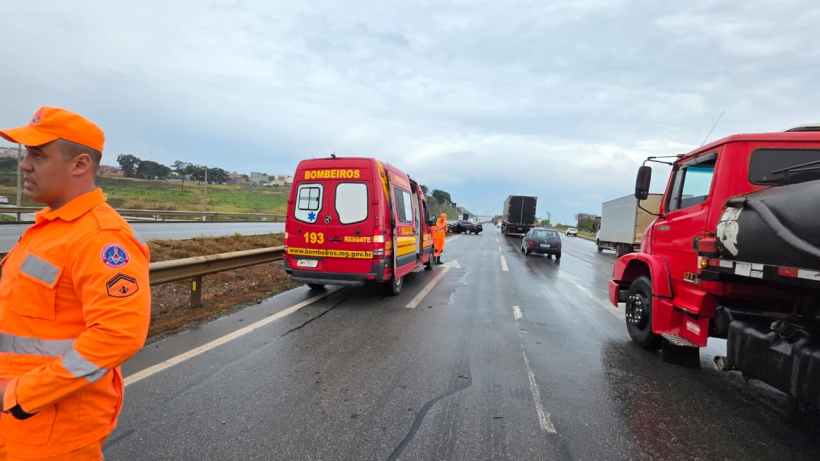 Caminhão vermelho e veículo de emergência dos bombeiros em uma estrada molhada, com bombeiros trabalhando na cena.