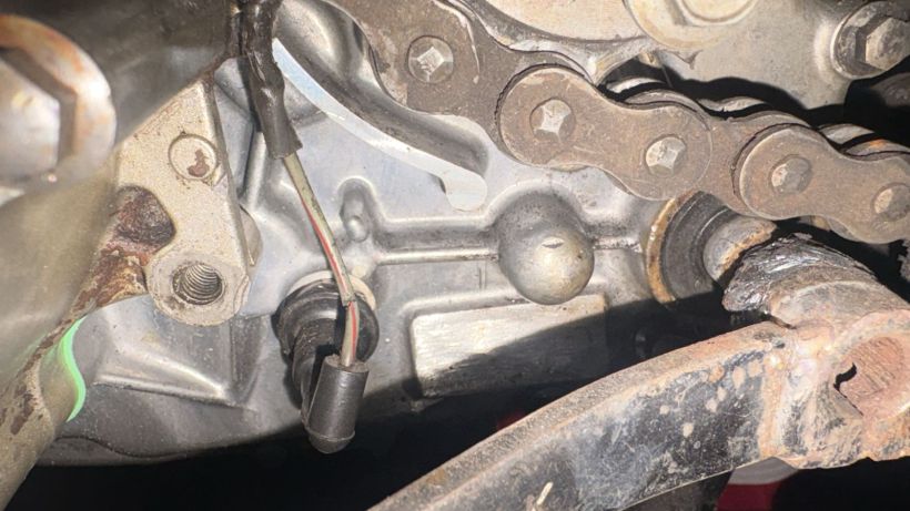 Visão detalhada de um componente mecânico com uma corrente, cabos e partes metálicas, apresentando sinais de desgaste e sujeira.