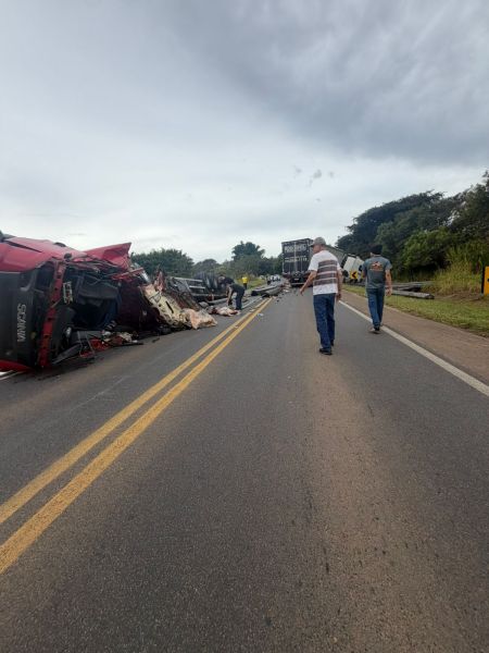 Acidente de caminhões na estrada com um veículo virado e pessoas caminhando ao longo da pista.