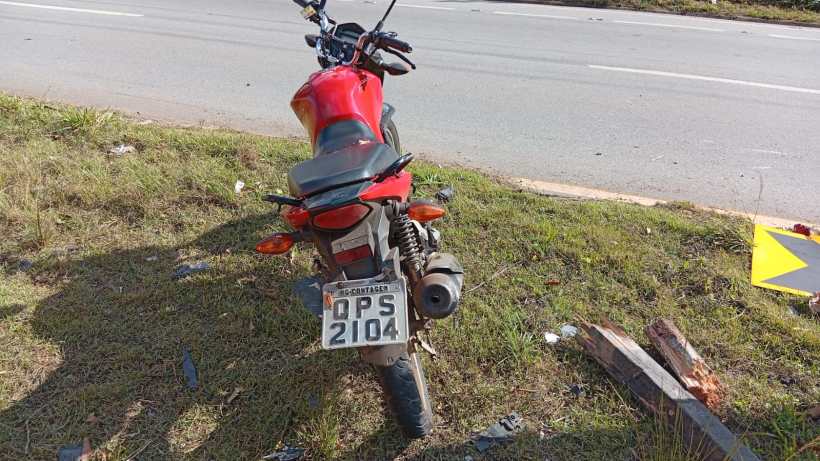 Moto vermelha parada à beira da estrada, com placas visíveis.