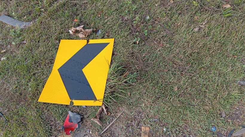 Placa de advertência de curva à esquerda caída em uma área gramada.