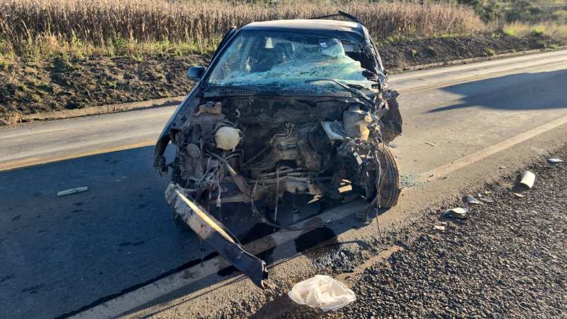 Carro com a frente danificada após um acidente, parado na estrada ao lado de um campo.