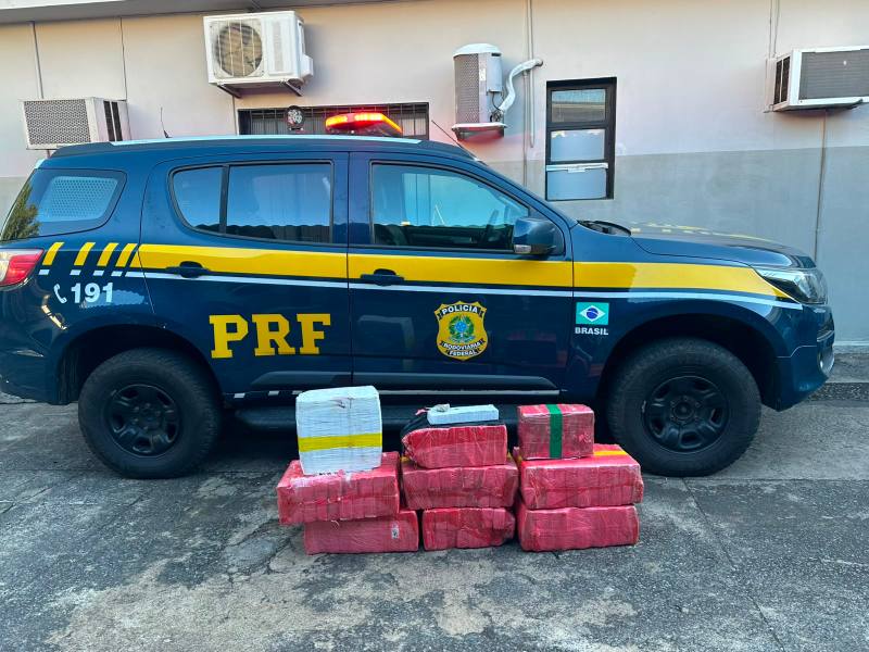 Viatura da PRF estacionada ao lado de pacotes de carga suspeita com embalagem vermelha.