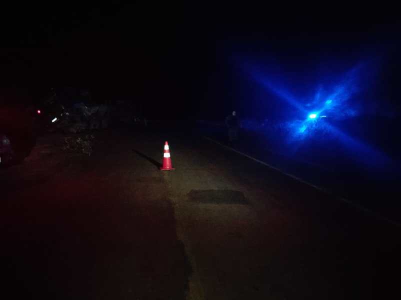 Estrada escura à noite com um cone sinalizador no centro e luzes azuis ao fundo.