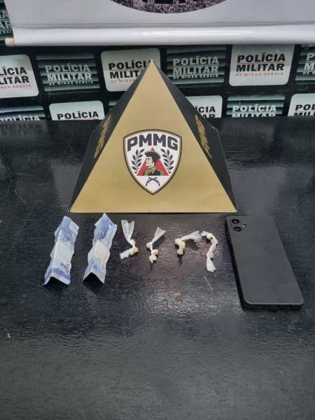 Uma pirâmide com o emblema da PMMG, acompanhada de pacotes e objetos suspeitos organizados ao lado e um celular preto.