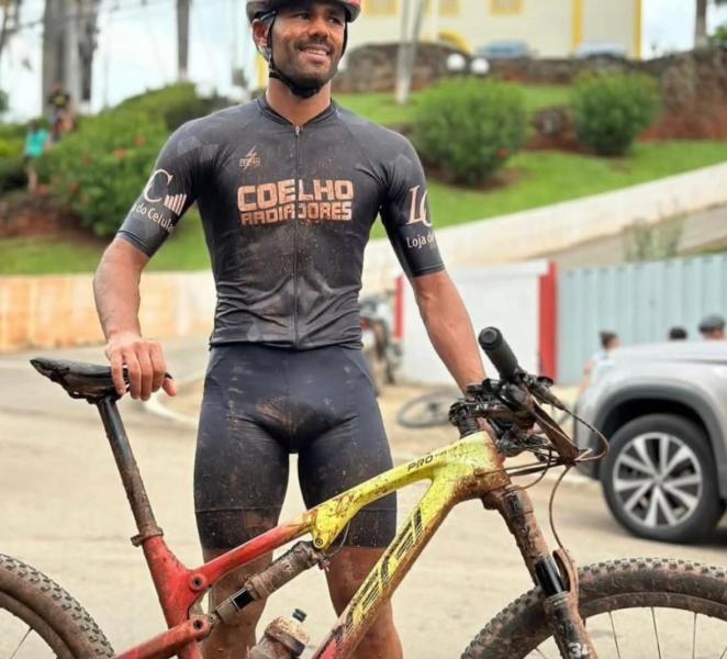 Ciclista suado e sorridente segurando sua bicicleta de montanha suja após uma competição.