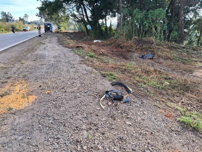 Foto mostrando uma estrada com uma pista de cascalho ao lado, vegetação e alguns objetos abandonados no chão.