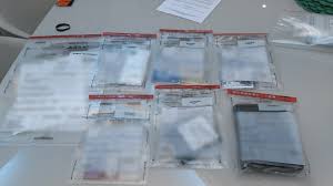 Vários pacotes plásticos transparentes organizados sobre uma mesa, cada um contendo diferentes itens ou documentos.