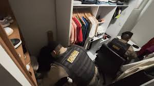 Policiais revistando um closet com roupas e calçados.